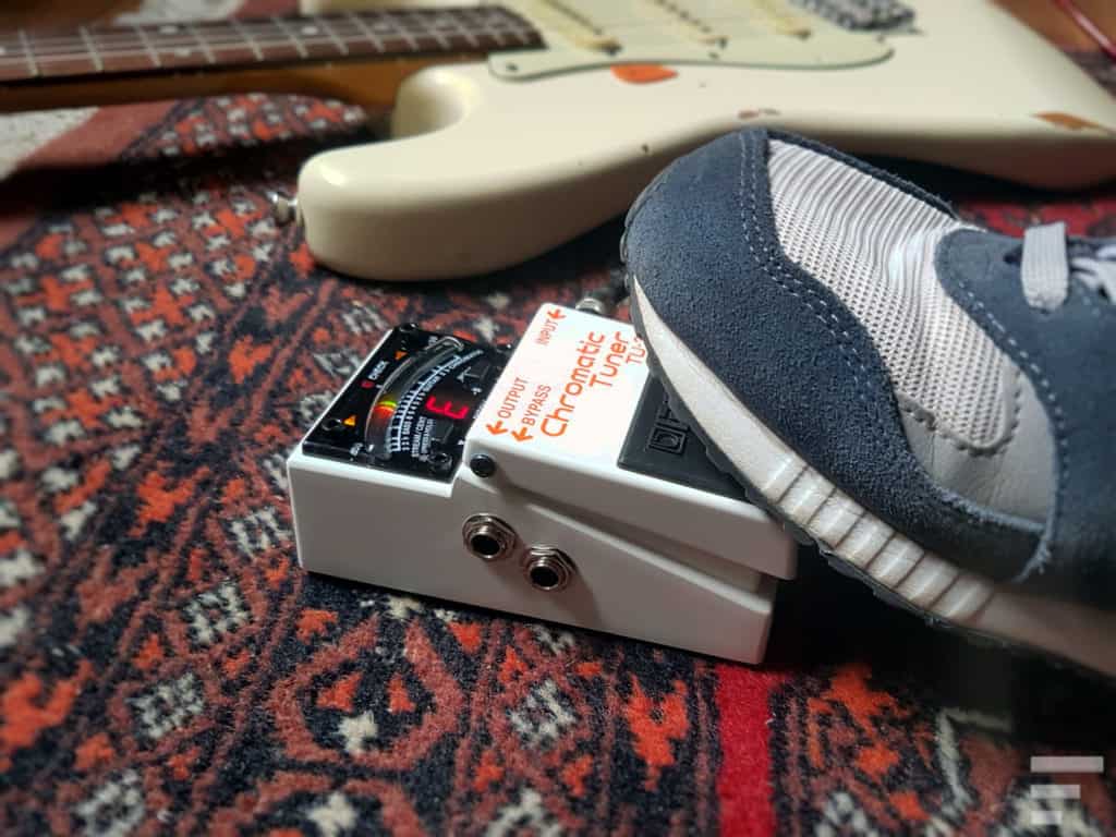 Boss TU-3 guitar tuner activated with a foot, with a Stratocaster guitar sitting in the background. 
